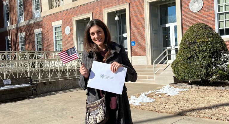 Claire Speaks se tient devant un bâtiment de l'administration américaine avec un drapeau américain et son certificat de citoyenneté.